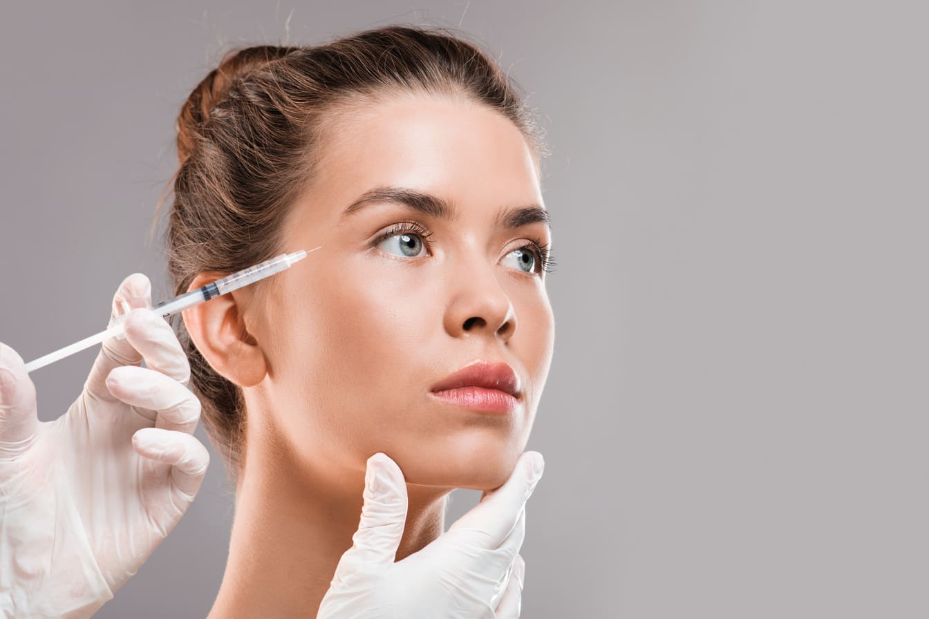 Young beautiful woman getting botox injection over grey background